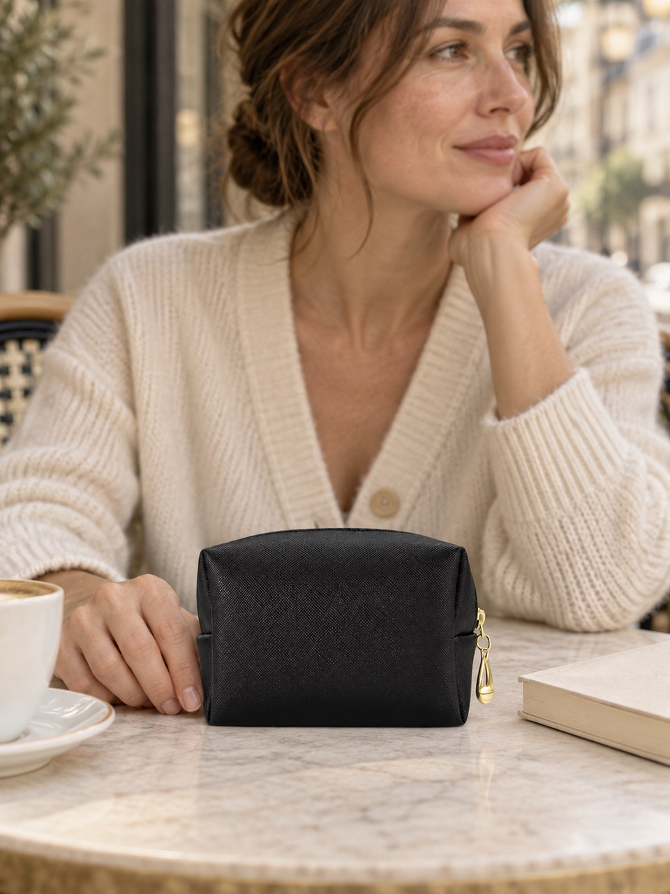 Pochette noire texturée à fermeture dorée sur une table de café.